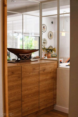 Enjoy a serene view of lush greenery from the large window in this stylish room, featuring a unique cabinet, artwork, and a vase with fresh flowers.