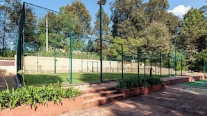 Ein Tennisplatz, umgeben von Bäumen und einem wolkenlosen Himmel, mit einem grünen Zaun und einem Netz.