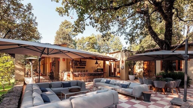 Eine Terrassengruppe im Freien mit Schachbrettboden, grauen Sofas und Sonnenschirmen, die Schatten spenden.