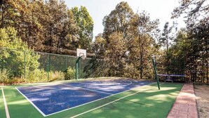 Ein Tennisplatz im Freien mit grüner und blauer Spielbelag, umgeben von Bäumen und einem Zaun.