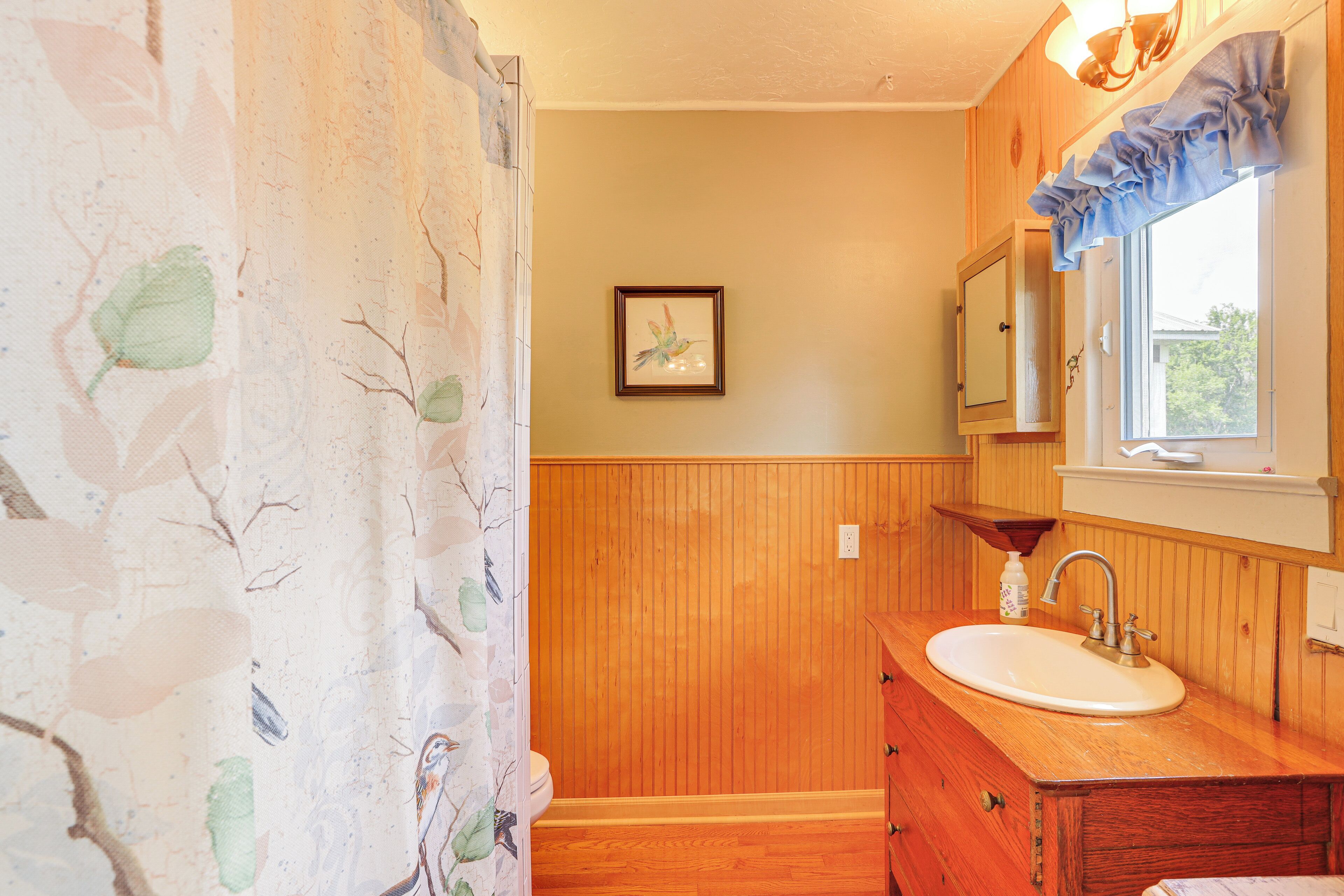 Une salle de bain avec des lambris en bois, un lavabo avec un miroir et un tableau encadré au mur.