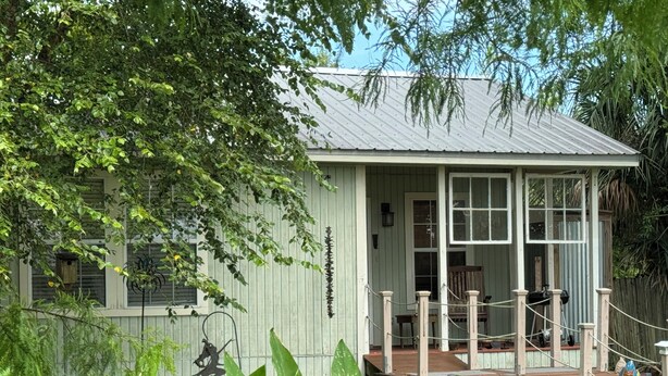 A small, single-story wooden house with a porch and a fenced yard. - Artist studio with comfy living accommodations. (Bay St. Louis)