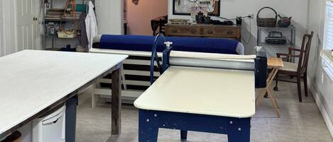 Una habitación con una mesa larga, una mesa azul con cubierta blanca, un televisor instalado en la pared y un techo de madera.