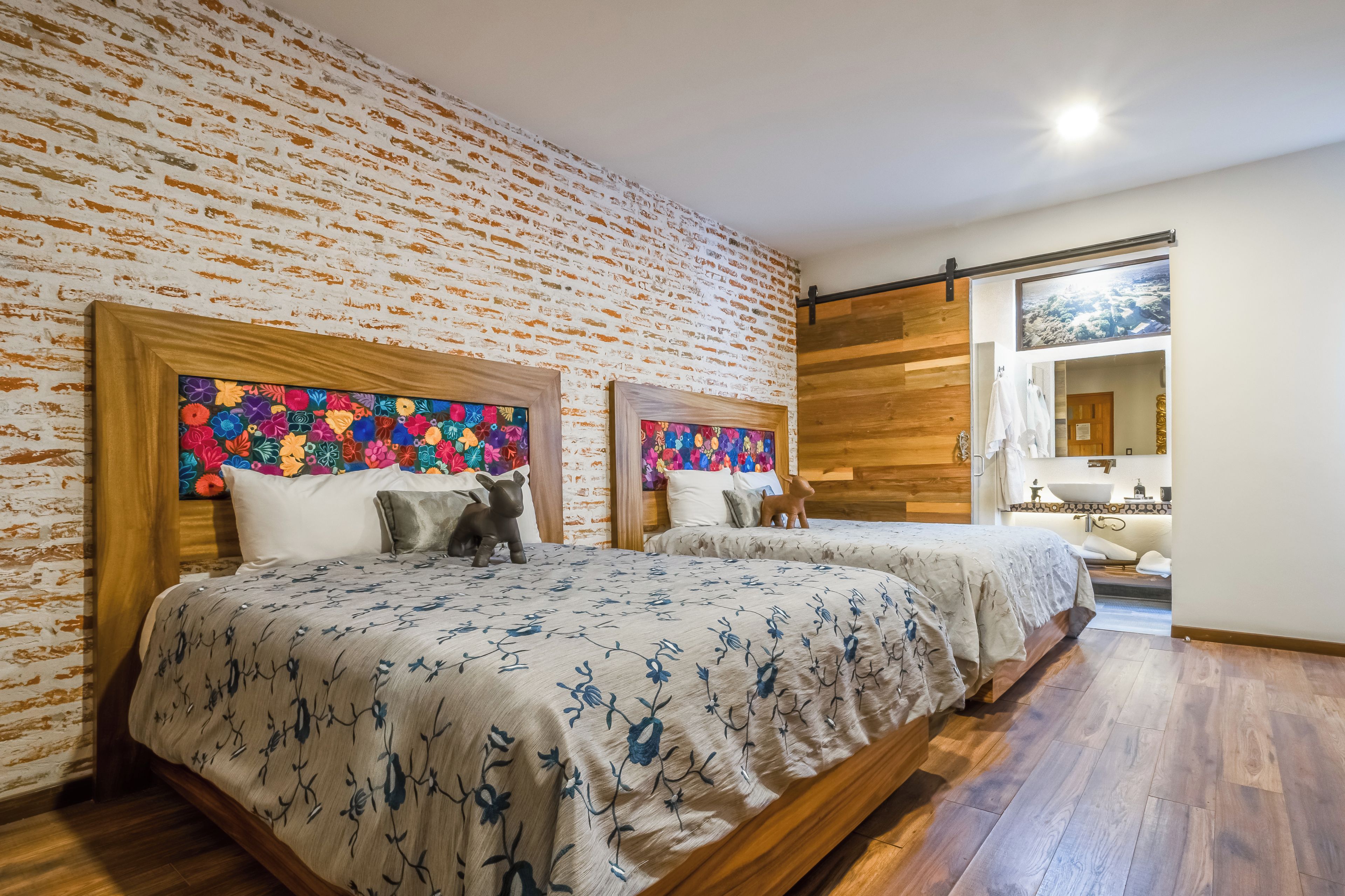 Habitación de hotel con dos camas, pared de ladrillo y suelo de madera.