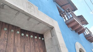 Een gevel van een gebouw met een blauwe muur, een houten deur met decoratieve schelpen en een balkon met houten leuningen.