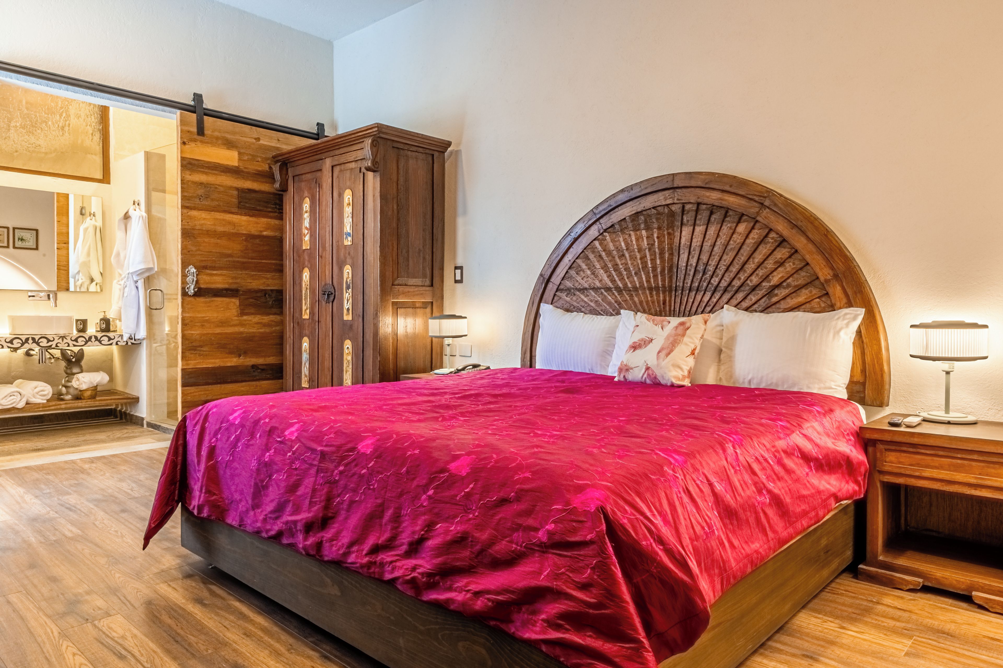 A bedroom with a large bed, wooden wardrobe, and a mirror.