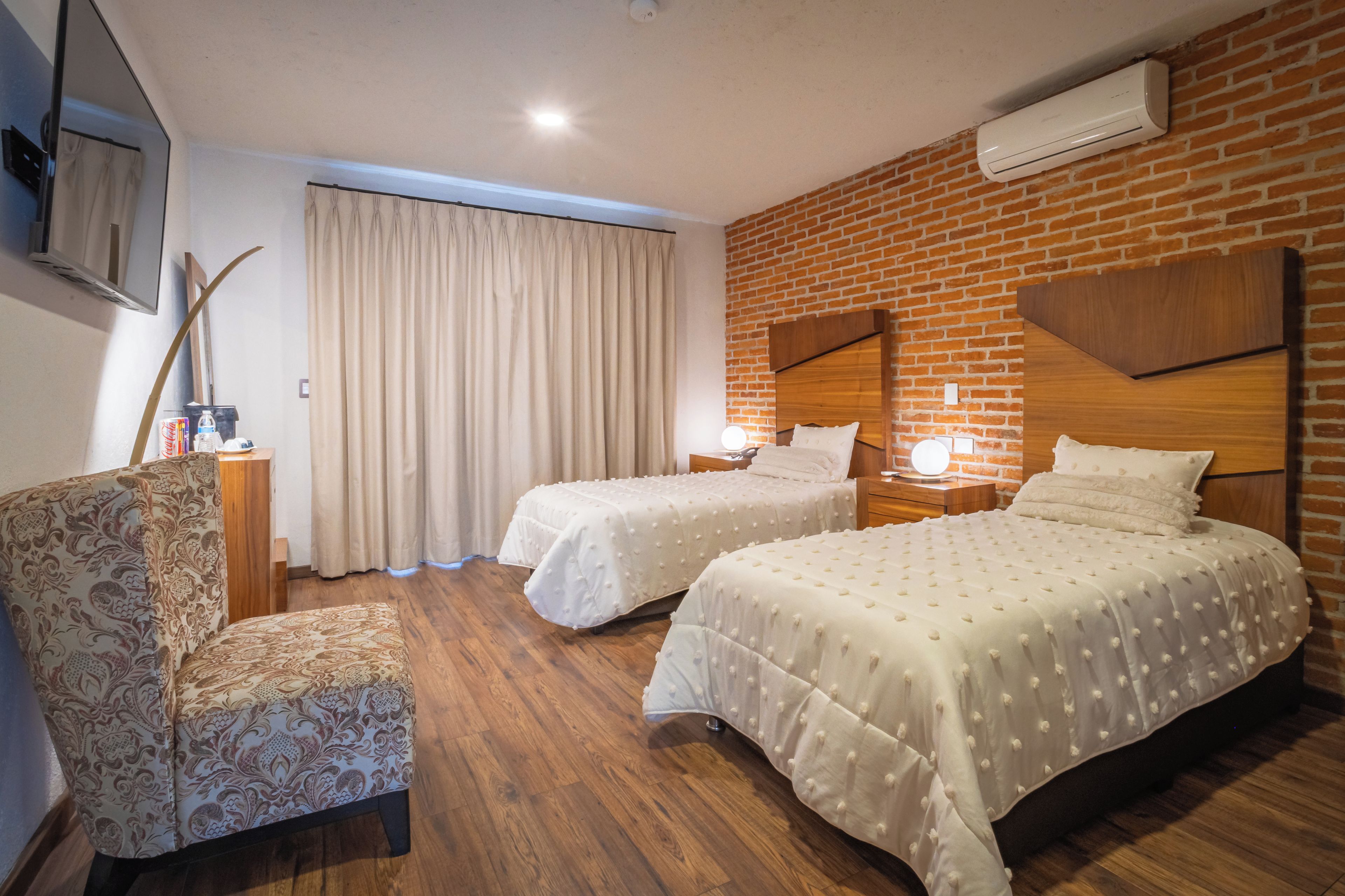 Ein Hotelzimmer mit zwei Betten, einem Schreibtisch, einem Sessel und einer Ziegelwand.