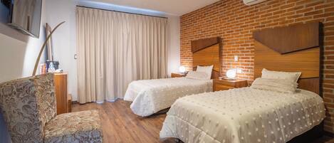 Ein Hotelzimmer mit zwei Betten, einem Schreibtisch, einem Sessel und einer Ziegelwand.