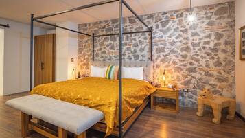 A four-poster bed with a bench, a stone wall, a wooden nightstand, and a small animal sculpture.