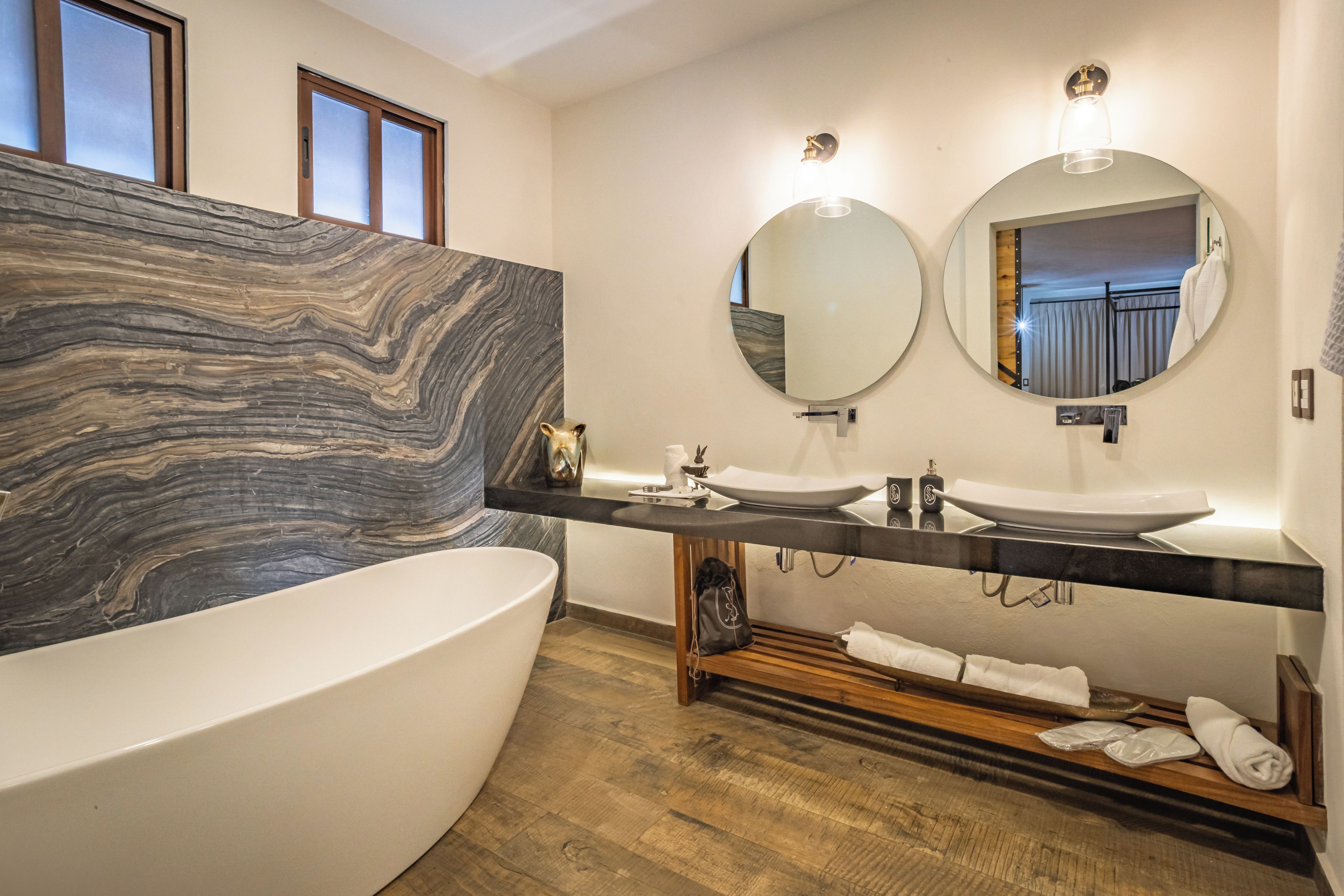 Une salle de bain moderne avec un meuble-lavabo en marbre, une baignoire sur pieds et deux miroirs fixés au mur.