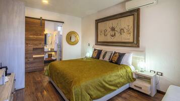 A hotel room with a large bed, a bedside table with a lamp, a wall-mounted air conditioner, and a framed artwork above the bed.