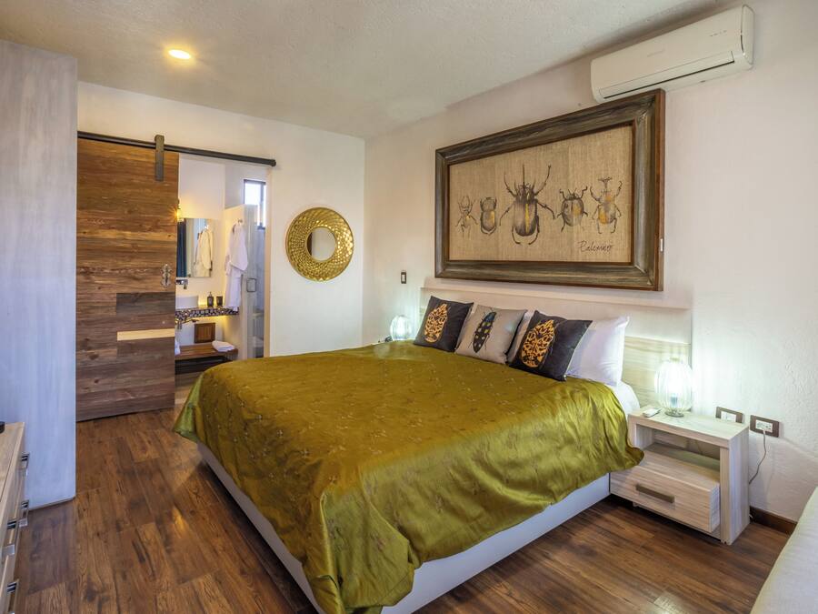 Habitación de hotel con una cama grande, una mesita de noche con lámpara, aire acondicionado de pared y una obra de arte enmarcada sobre la cama.