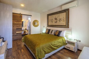 Habitación de hotel con una cama grande, una mesita de noche con lámpara, aire acondicionado de pared y una obra de arte enmarcada sobre la cama.
