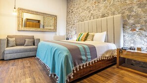 A bedroom with a stone wall, a bed with a striped blanket, a wooden nightstand, and a sofa. - Hotel Casa Chanehque (San Pedro Cholula)