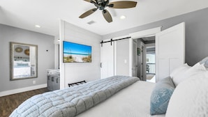 Et soveværelse med en seng, loftventilator, et vægmonteret TV og en dør, der fører ud til en balkon.