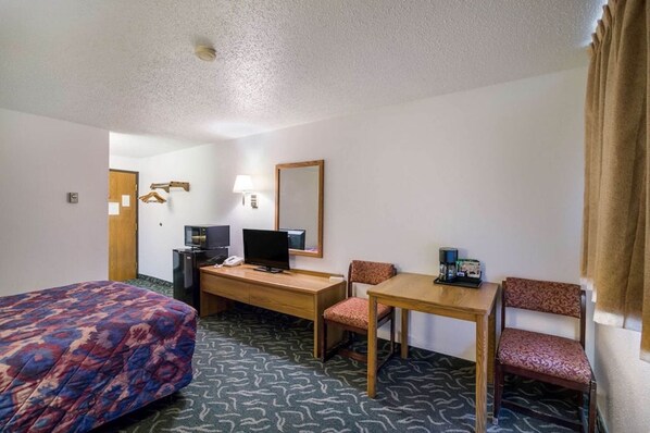 A hotel room with a bed, a desk with a computer, a chair, a table, and a lamp.