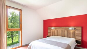 Ein Schlafzimmer mit großem Fenster, roter Akzentwand und Bett mit Kopfteil.