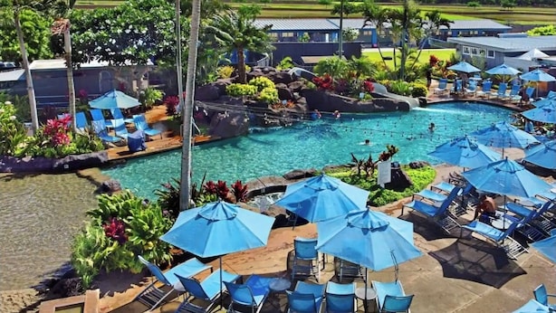 Un espace piscine agrémenté de chaises longues et de parasols, entouré de plantes tropicales et offrant une vue sur des collines lointaines.