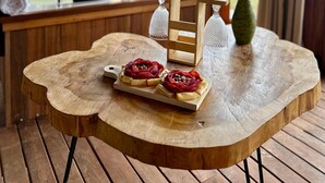 A wooden table with a rustic design, a wooden chair, a glass vase, and a tray with food items. - Ecoedén Glamping (Guatapé)
