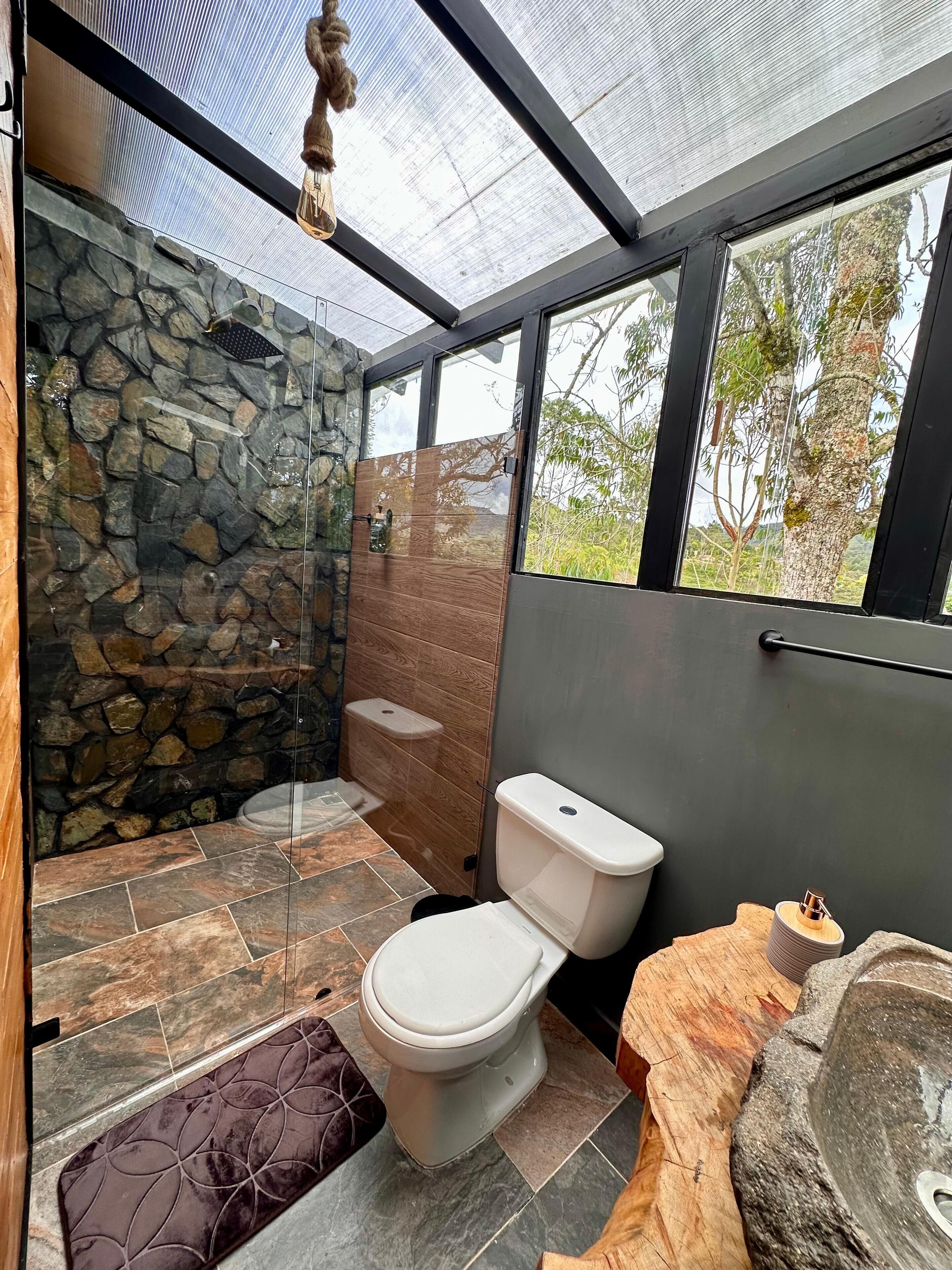 A modern bathroom with a stone wall, a glass shower enclosure, and a toilet.