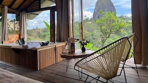 A wooden deck with a hot tub, a chair, and a table with a plant. - Ecoedén Glamping (Guatapé)