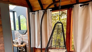 A wooden ceiling with a hanging chair, a small table with a sink, and a window with curtains. - Ecoedén Glamping (Guatapé)