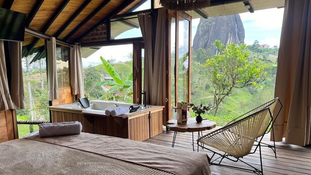 A bedroom with a large bed, a wooden desk, a chair, and a view of the outdoors. - Ecoedén Glamping (Guatapé)