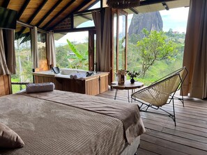 Ein Schlafzimmer mit einem großen Bett, einem Holztisch, einem Stuhl und Blick ins Freie.