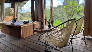 A wooden deck with a hot tub, two wicker chairs, and a table with a plant and a bottle. - Ecoedén Glamping (Guatapé)