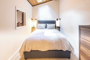 A bedroom with a bed, bedside lamps, a mirror, and a wooden dresser.