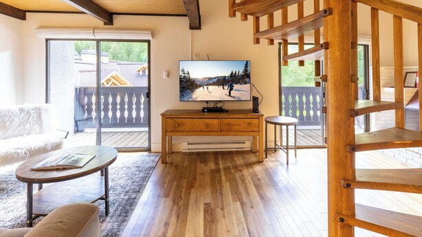 Un soggiorno accogliente con una panca in legno, un televisore su un mobile in legno e vista su un paesaggio innevato attraverso una porta scorrevole in vetro.