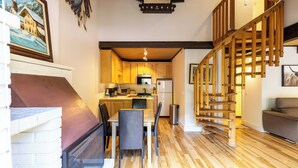 Una cucina moderna con mobili in legno, un tavolo da pranzo e sedie. Una scala con ringhiere in legno conduce a un livello superiore.