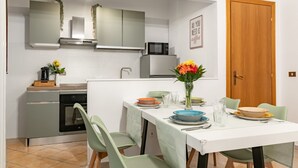 Une cuisine compacte équipée d’un four à micro-ondes, d’une cuisinière et d’un évier. On y trouve une table à manger avec des chaises et un vase de fleurs.