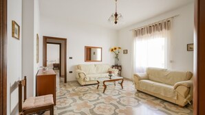 Ein Wohnzimmer mit einer Couch, einem Sessel, einem Couchtisch, einem Spiegel und einer Blumenvase.