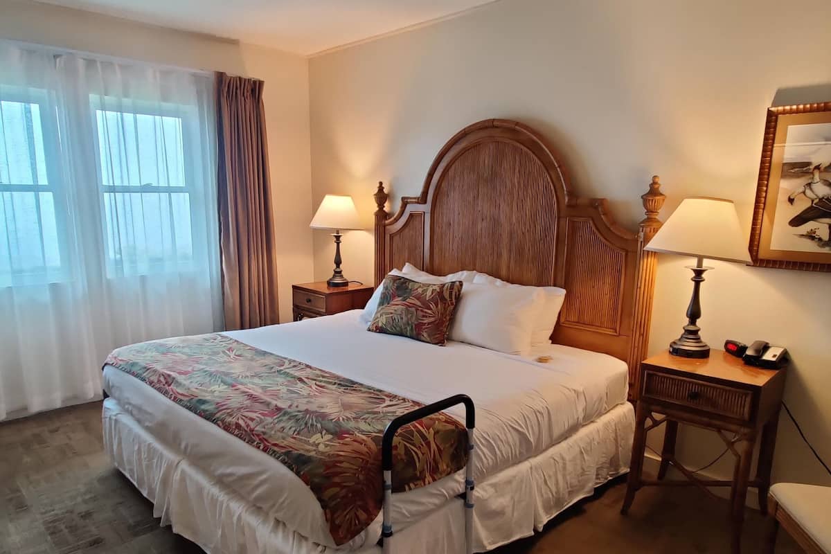 A neatly made bed with a floral bedspread, two bedside lamps, a wooden headboard, and a nightstand with a telephone and a small table.