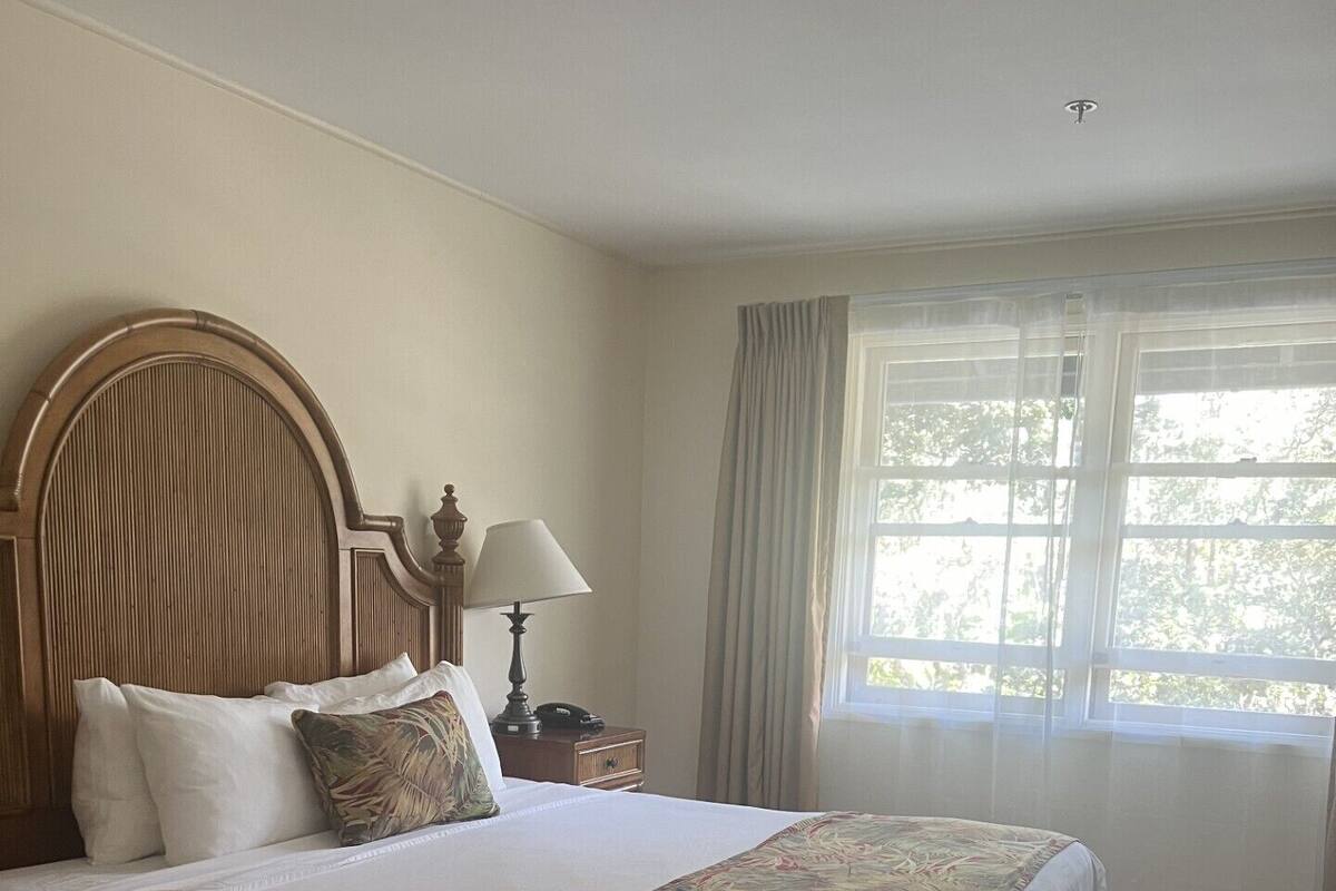A neatly made bed with a floral bedspread, a wooden headboard, and a bedside table with a lamp.