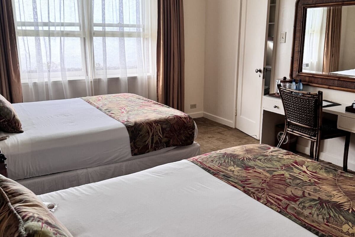 A hotel room with two beds, a desk, a chair, a mirror, and a window with curtains.
