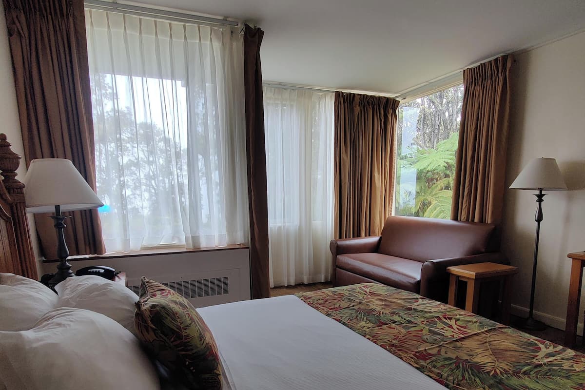 A hotel room with a large bed, a brown leather chair, a small table, and a lamp.