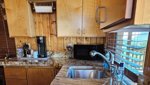 A kitchen with granite countertops, stainless steel sink, wooden cabinets, and a microwave. - The Peacemaker Cabin: Cozy cabin in enjoyable Apple Valley with AC (Apple Valley)