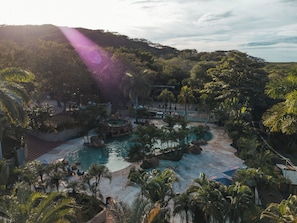 Un resort con diverse piscine circondate da palme e con montagne sullo sfondo.