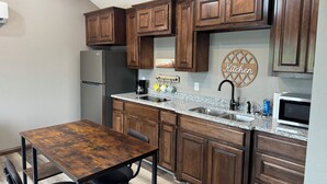 Une cuisine moderne avec des meubles en bois, un plan de travail en granit, un réfrigérateur en acier inoxydable et un coin repas comprenant une table et des chaises en bois.