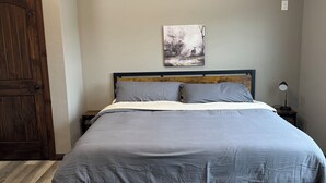 Une chambre à coucher avec un lit, une porte en bois, un tableau accroché au mur et une table de chevet avec une lampe.