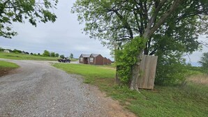 Un chemin de gravier menant à une maison entourée d’une clôture en bois et bordée d’un arbre.