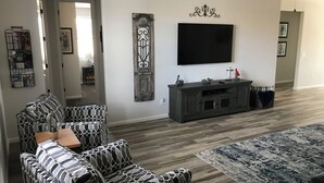 A living room with a sofa, a TV, a decorative wall piece, and a patterned rug. - Cozy Casa Bliss: 3 bedroom Desert Home (Casa Grande)