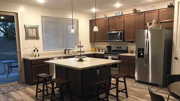A modern kitchen with a central island, stainless steel appliances, wooden cabinets, and pendant lighting. - Cozy Casa Bliss: 3 bedroom Desert Home (Casa Grande)