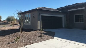 A residential building with a garage, a small garden area, and a clear blue sky. - Cozy Casa Bliss: 3 bedroom Desert Home (Casa Grande)