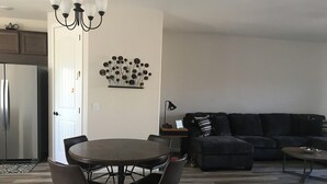 A modern living room with a round dining table, dark sofas, and a chandelier. - Cozy Casa Bliss: 3 bedroom Desert Home (Casa Grande)