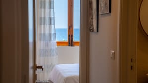 Een kamer met een bed, een raam met uitzicht op zee en een deur naar een andere kamer.