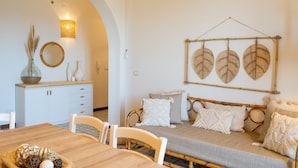 Een kamer met een eettafel, stoelen, een bed met wit beddengoed, een bladdecoratie aan de muur en een spiegel.
