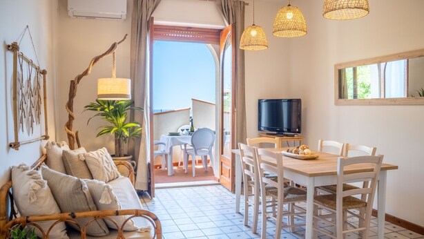 Een gezellige woonkamer met een bank, een eettafel met stoelen, een televisie en een balkon met uitzicht.